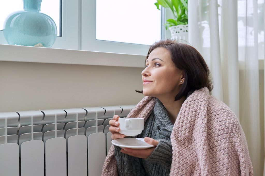 Winter season, woman warming up near home heating radiator